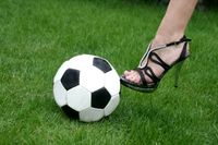 Bild eines Frauenbeins mit hohen Schuhen, die einen Fußball tritt